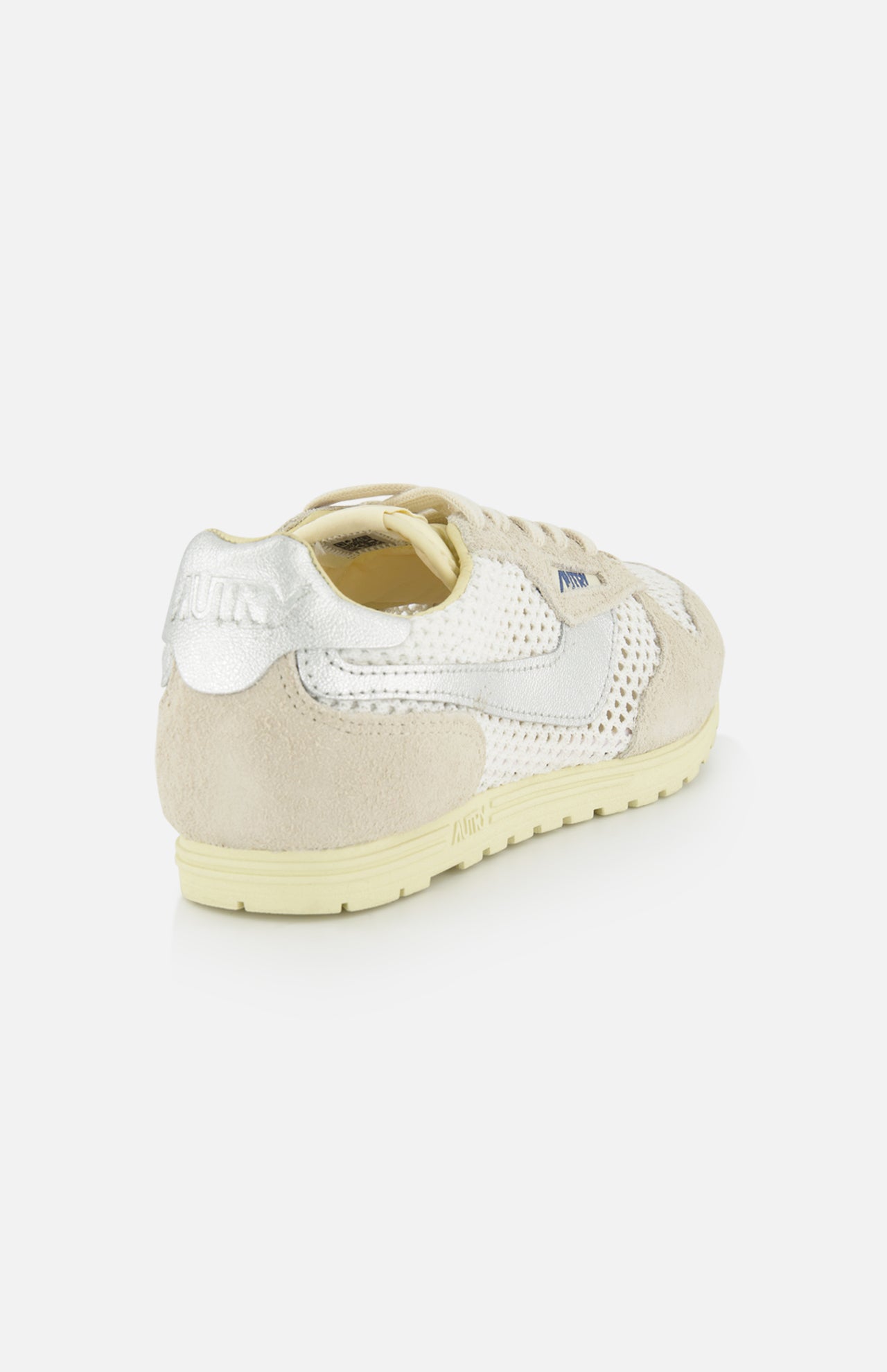 The AUTRY Windspin Low Knit Sneaker features a beige and silver design with a suede heel, mesh panels, and a cream sole, offering vintage style. Shown angled from the back on a white background.