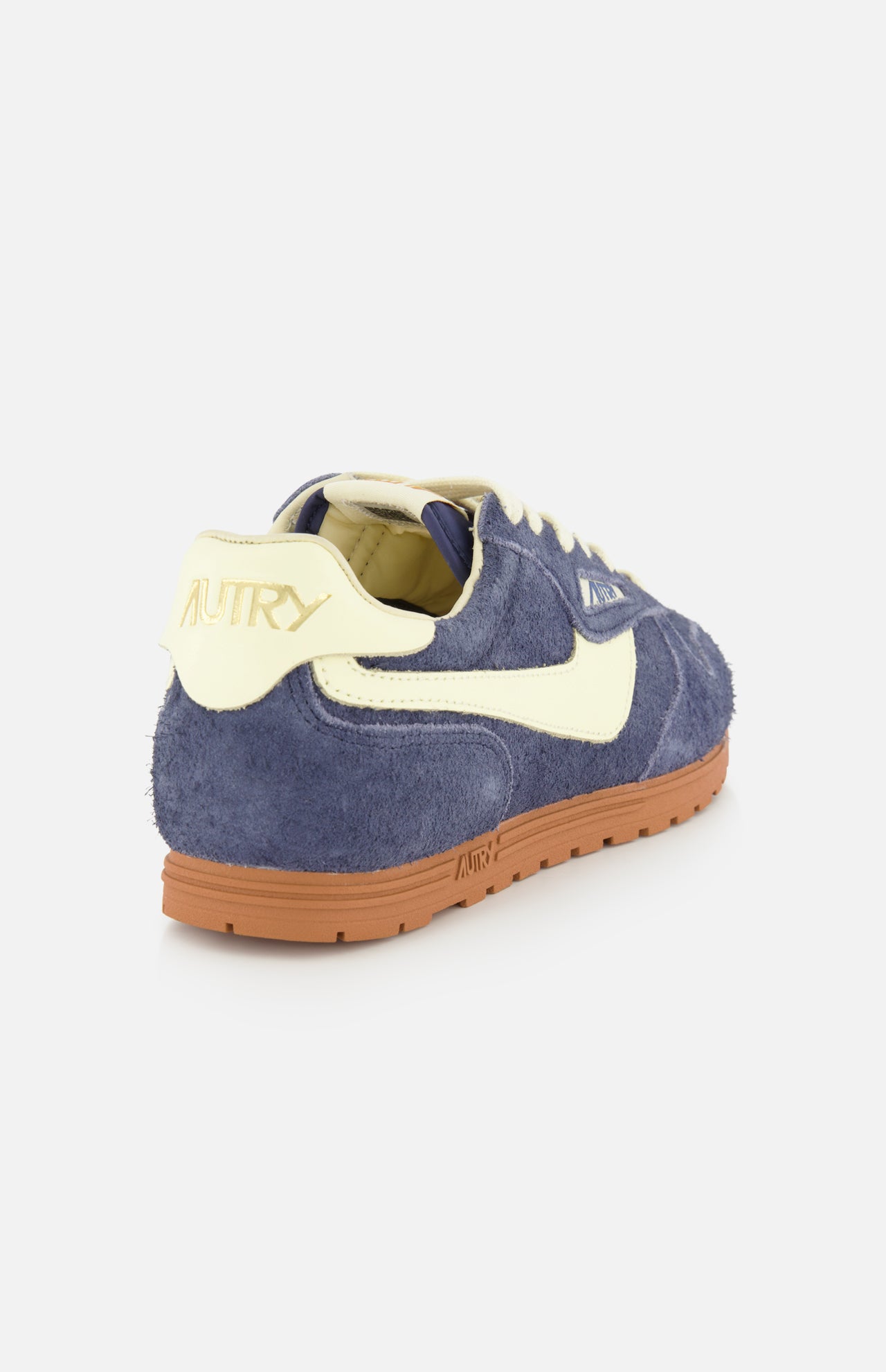 The AUTRY Windspin Low Suede Sneaker is showcased against a plain white background, featuring dark blue suede for vintage appeal, a cream heel tab with AUTRY branding, a cream side stripe, crisp white laces, and a brown rubber sole inspired by 60s style.