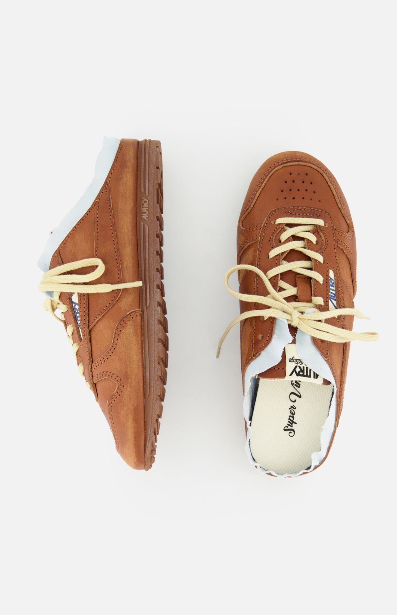 The AUTRY Windspin Leather Mule Sneaker, a brown slip-on with cream laces, is shown on a white background—one sneaker upright and the other on its side.