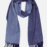 The Arran Reversible Scarf by BEGG & CO is a luxurious cashmere accessory made in Scotland, showcasing two-toned blue hues with light blue on one side and dark blue on the other. Finished with fringe at both ends, the scarf is elegantly displayed laid flat on a white background.