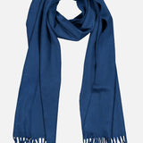 The BEGG & CO Arran Solid Scarf, a long blue cashmere accessory with fringed ends crafted in Scotland, is shown laid flat in a loop shape against a white background.
