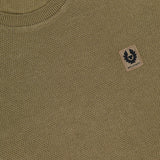 Close-up of a BELSTAFF Coast Knitted Sweater in olive green cotton-silk knit, featuring a ribbed crew neck, small beige logo patch with black emblem on the chest, and an inner label reading “Belstaff Silk Cotton.”.