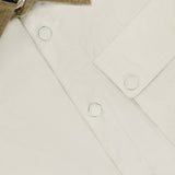 Close-up of the BELSTAFF Water Repellent Ground Jacket in cream, featuring a tan corduroy collar, white buttons, front chest pocket, and a visible black and gold inner label near the collar.