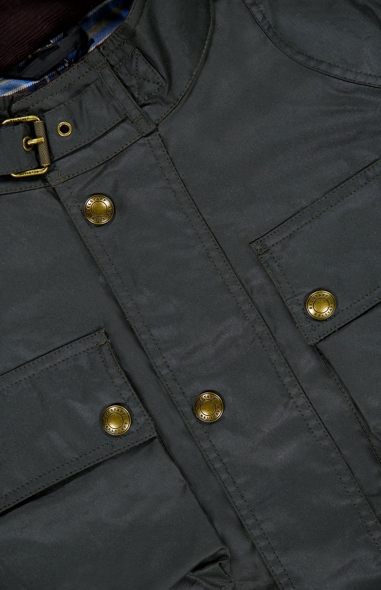 Close-up of the BELSTAFF Racemaster Waxed Cotton Jacket in dark green, featuring brass snap buttons, two flap pockets, and a buckle detail near the collar, highlighting its iconic style.