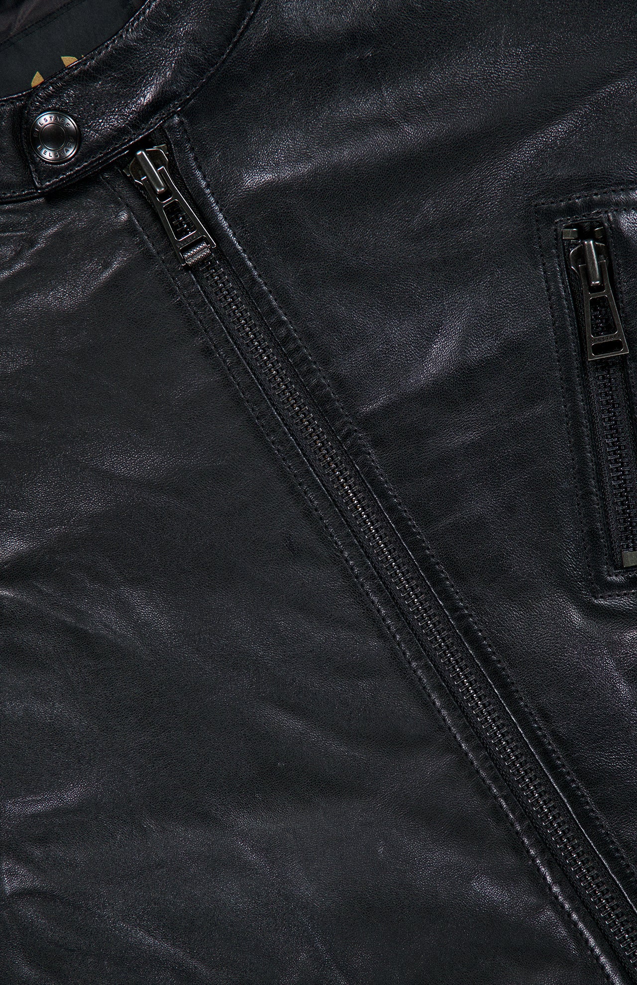 Close-up of the BELSTAFF V Racer Jacket in black leather, featuring a snap button at the collar, two parallel zippers, and visible pocket stitching that highlights the supple leather texture and minimalist design details.