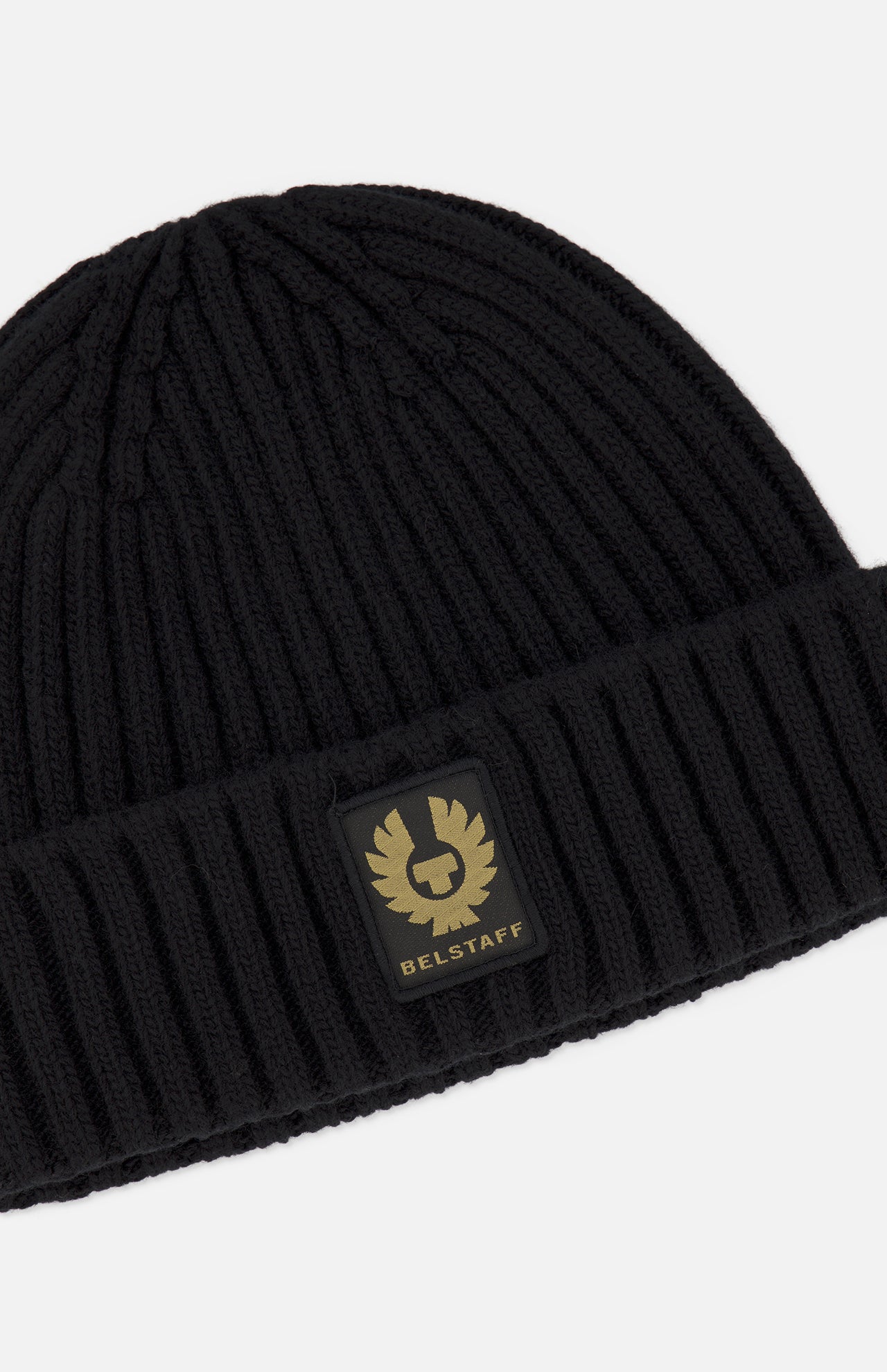 The BELSTAFF Watch Beanie Hat is a black ribbed knit wool beanie with a folded brim, adorned with a rectangular black and gold BELSTAFF logo patch on the front.
