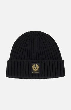 The BELSTAFF Watch Beanie Hat is a black ribbed knit wool beanie with a folded brim, accented by a rectangular black and gold BELSTAFF logo patch on the front.