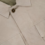 Close-up of the BELSTAFF Waymark Suede Overshirt in beige goat suede, showcasing a button, visible seams, partial shirt collar, and chain at the inside neckline—a perfect lightweight layering piece.