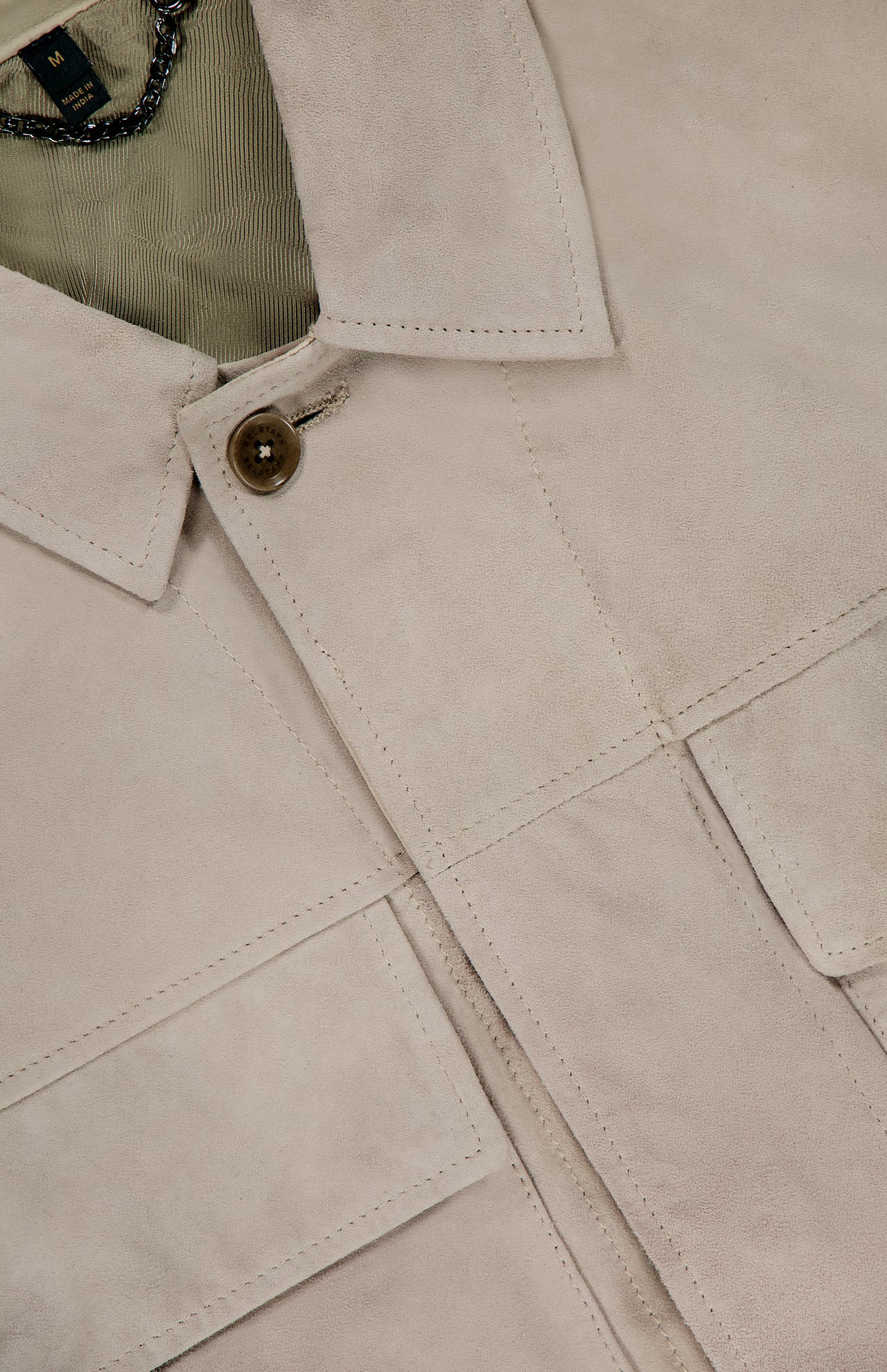Close-up of the BELSTAFF Waymark Suede Overshirt in beige goat suede, showcasing a button, visible seams, partial shirt collar, and chain at the inside neckline—a perfect lightweight layering piece.
