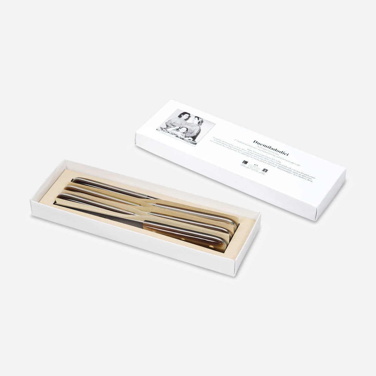 A white box displays four shiny metal forks, neatly arranged, with the lid beside it featuring a black and white photo and text. Complements the Berti Cutlery Duemiladodici “Two-Twelve” Table Knife (6pc) set. Plain, light background.