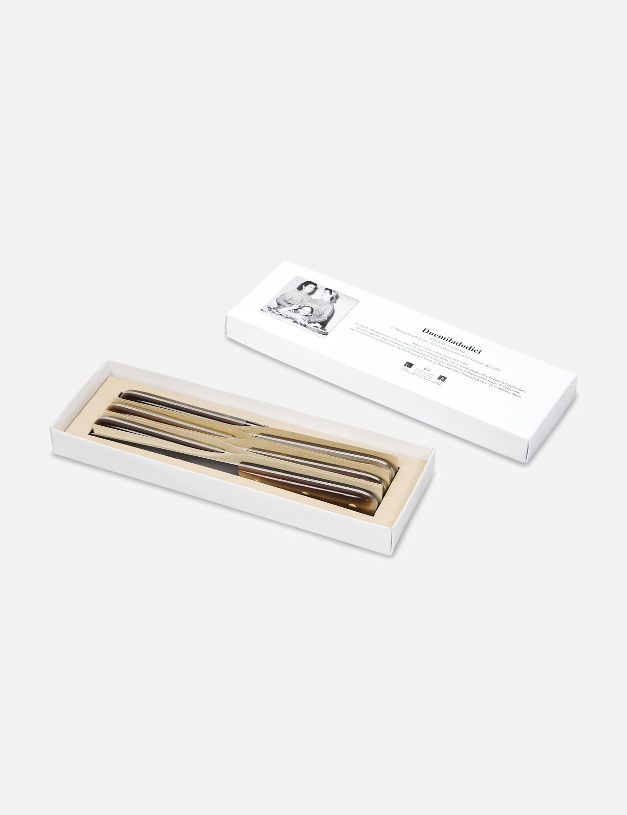 A white box displays four shiny metal forks, neatly arranged, with the lid beside it featuring a black and white photo and text. Complements the Berti Cutlery Duemiladodici “Two-Twelve” Table Knife (6pc) set. Plain, light background.