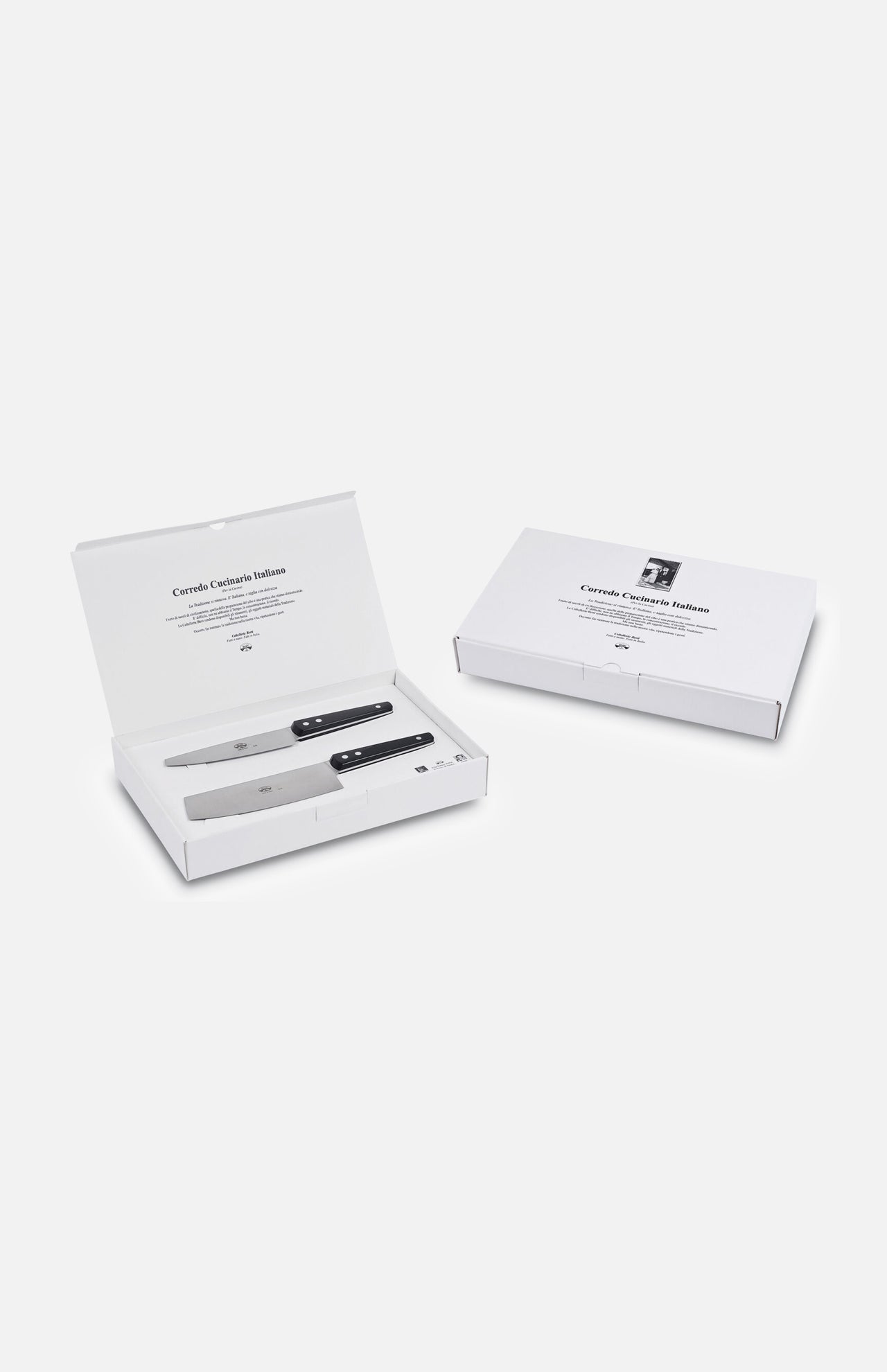 Two white boxes—one open, one closed—contain the Berti Cutlery Kitchen Knife Kit (Set of 2) with black handles. The open box displays the knives in slots, with master knife makers' text printed inside the lid.
