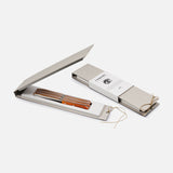 Two slim, beige Berti Cutlery boxes with string closures are shown. One is closed with a booklet on top; the other is open, displaying the Table Knife “Compendium” 6-piece set featuring elegant orange and brown striped handles.