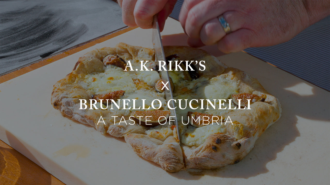 image with text "A.K. Rikk's Brunello Cucinelli A Taste of Umbria" image is of a fresh baked pizza being cut
