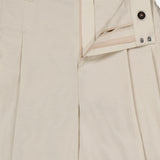 A close-up of BRUNELLO CUCINELLI's Cotton Poplin Deep Pleat A-Line Pant in light beige, featuring an open waistband, button and hook-and-bar closure, inner waistband details, and belt loops—expertly crafted in Italy.