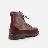 The Leather and Suede Ankle Boots by BRUNELLO CUCINELLI are Italian-crafted brown lace-up boots combining smooth leather and suede, set on a thick rubber sole. The image displays side and back views against a white background.