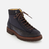The BRUNELLO CUCINELLI Suede Ankle Boots are shown on a white background, angled to display both the side and front. This classic lace-up style features a dark navy suede upper, brown laces, a brown sole, and black accents.