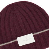 A rib-knit cashmere beanie in burgundy by BRUNELLO CUCINELLI, featuring a thin horizontal beige stripe and a white label with the brand name.