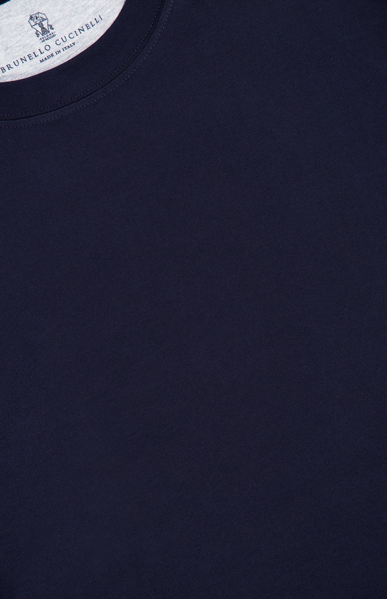 Close-up of the upper section of the BRUNELLO CUCINELLI Cotton Crewneck T-Shirt in dark navy blue, highlighting the collar and a partial label featuring “Brunello Cucinelli” and “Made in Italy” text against a white background. This slim-fit crewneck exemplifies refined craftsmanship and contemporary style.