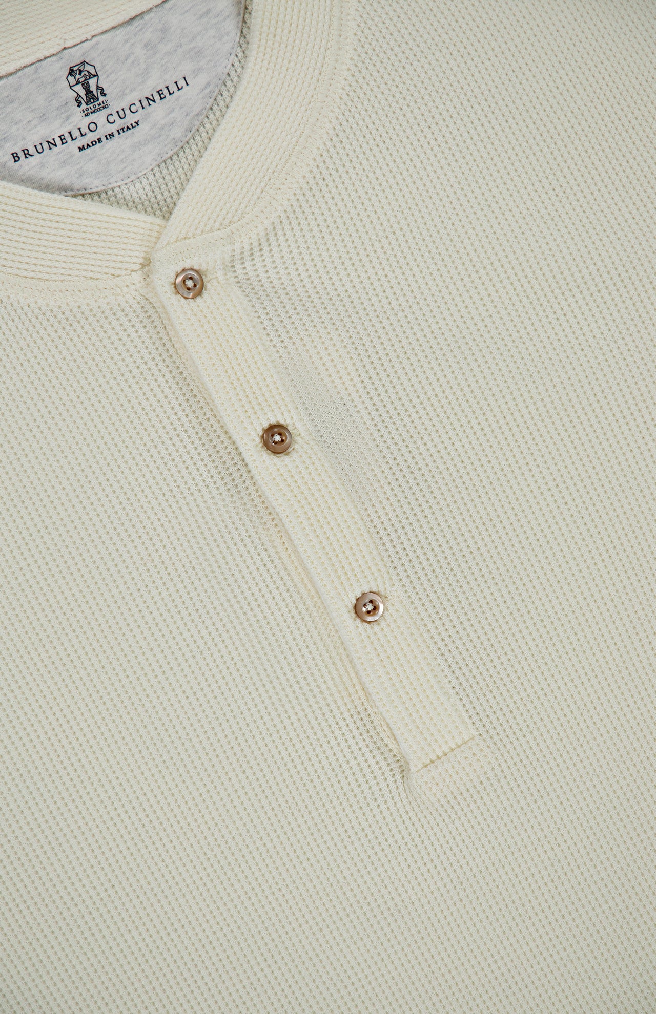 Close-up of a cream-colored Cotton Long Sleeve Henley T-shirt with a waffle knit, partial button placket, and three metallic buttons. The collar label shows BRUNELLO CUCINELLI, Made in Italy.