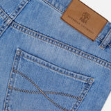 Close-up of Italian denim light blue Button Fly Denim Jeans from BRUNELLO CUCINELLI, featuring a back pocket with decorative stitching and a brown leather brand patch labeled BRUNELLO CUCINELLI on the waistband, highlighting the garment’s vintage treatment.