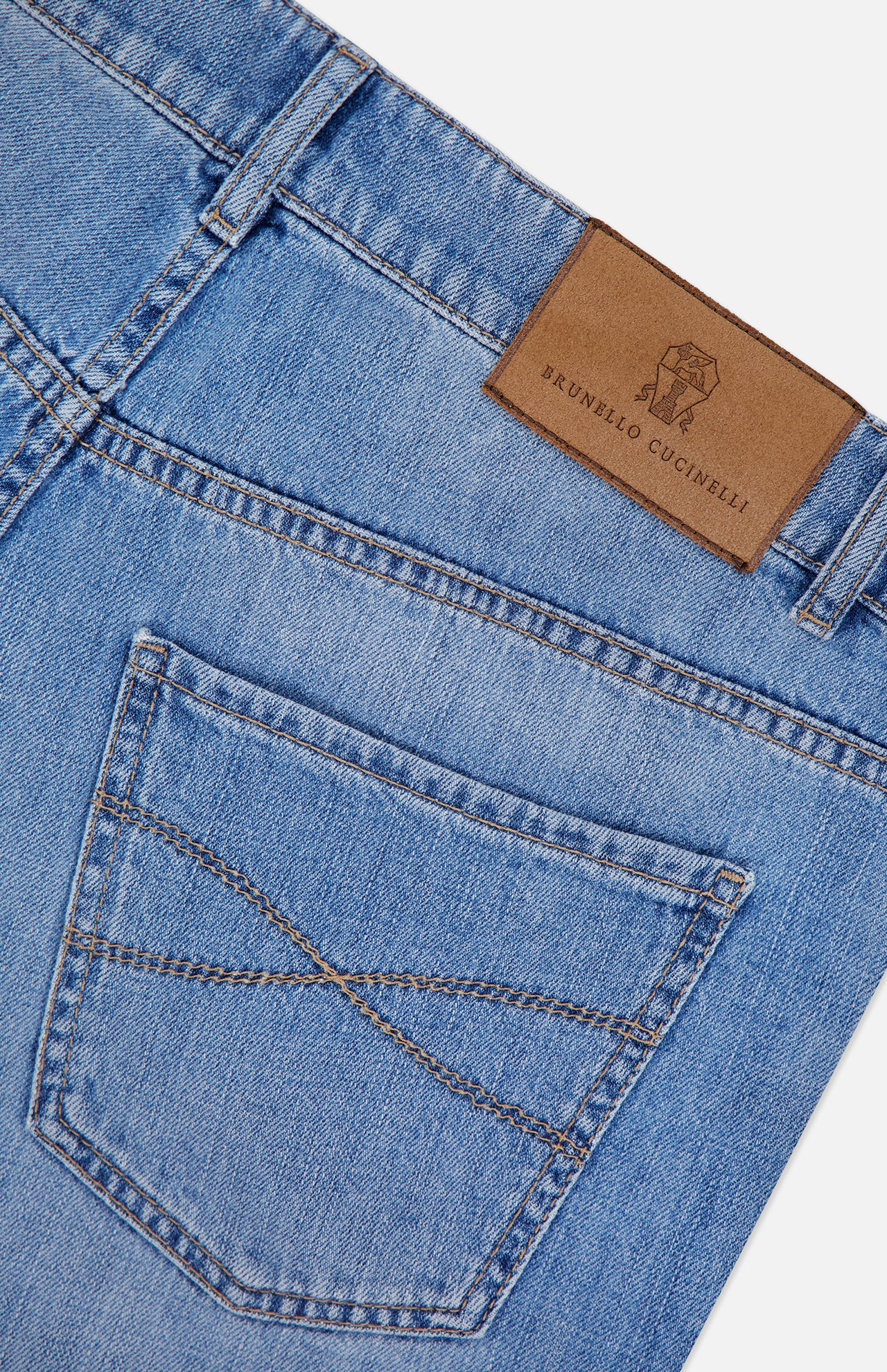 Close-up of Italian denim light blue Button Fly Denim Jeans from BRUNELLO CUCINELLI, featuring a back pocket with decorative stitching and a brown leather brand patch labeled BRUNELLO CUCINELLI on the waistband, highlighting the garment’s vintage treatment.