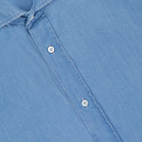 Close-up of a light blue wash BRUNELLO CUCINELLI Denim Button Down Shirt with white buttons, pointed collar, and a visible "Basic Fit" label inside the collar.