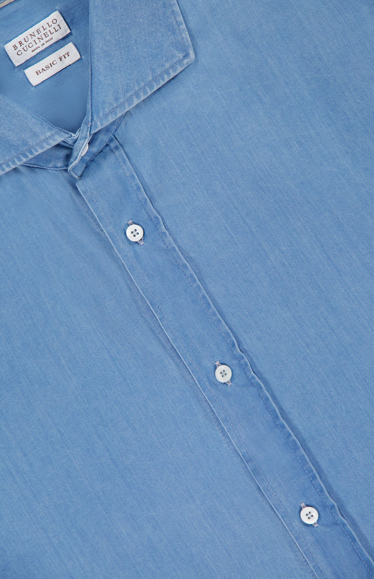 Close-up of a light blue wash BRUNELLO CUCINELLI Denim Button Down Shirt with white buttons, pointed collar, and a visible "Basic Fit" label inside the collar.
