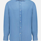 The BRUNELLO CUCINELLI Denim Button Down Shirt features a light blue wash, long sleeves, collar, white buttons, and a straight hem, shown against a plain white background.