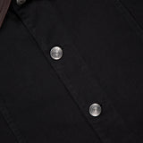 Close-up of the BRUNELLO CUCINELLI Denim with Leather Collar Jacket, featuring black denim, silver buttons, a brown leather collar, and a visible clothing label—showcasing timeless retro style.