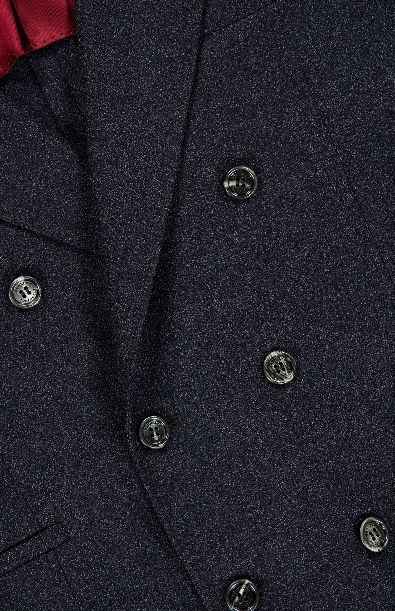 Close-up of the BRUNELLO CUCINELLI Double Breasted Suit Jacket in dark grey virgin wool, featuring six black buttons and a hint of red fabric at the top left corner.