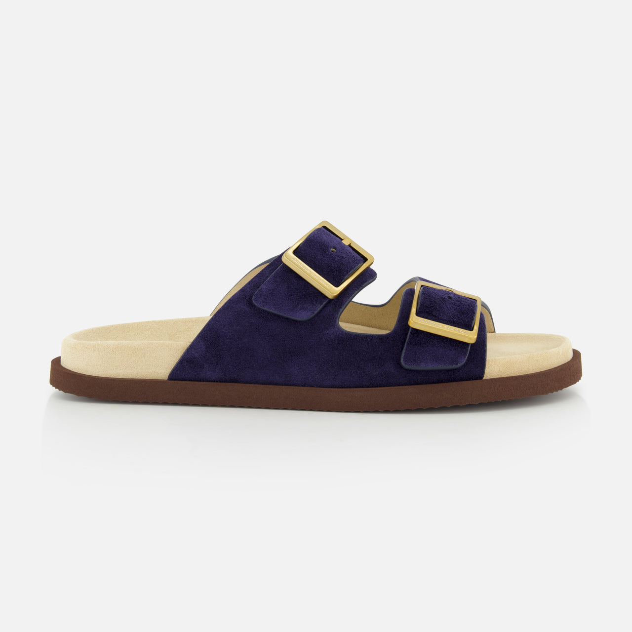 The BRUNELLO CUCINELLI Double Buckle Suede Sandals are slip-ons in navy with two wide straps, large gold buckles, a light beige footbed, and a flat brown sole, pictured in profile on a white background.