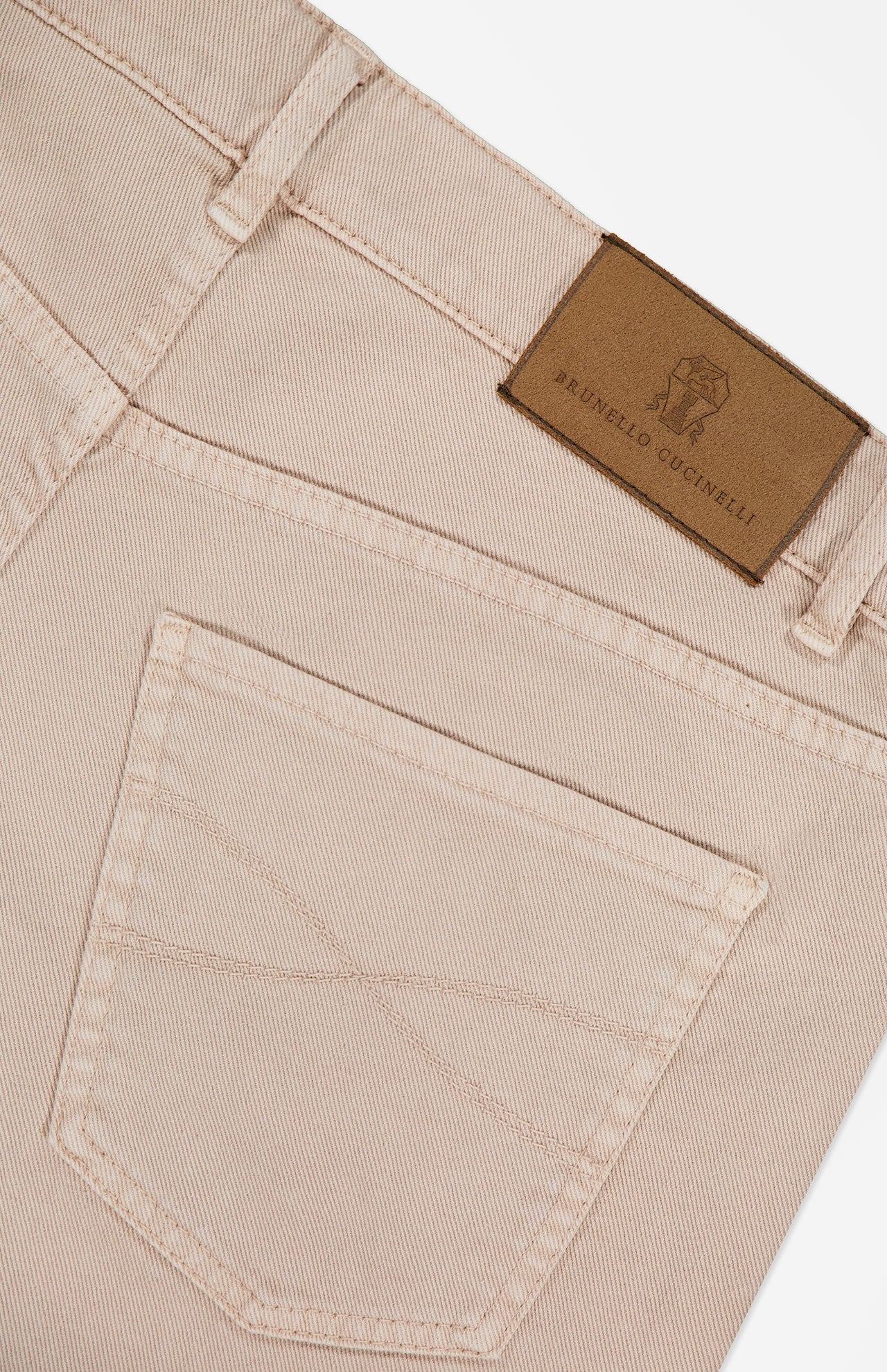 Close-up of the Button Fly Dyed Denim Pants in beige, expertly crafted from premium Italian denim by BRUNELLO CUCINELLI, highlighting the back pocket and waistband detailed with a brown leather patch embossed with the brand's logo.