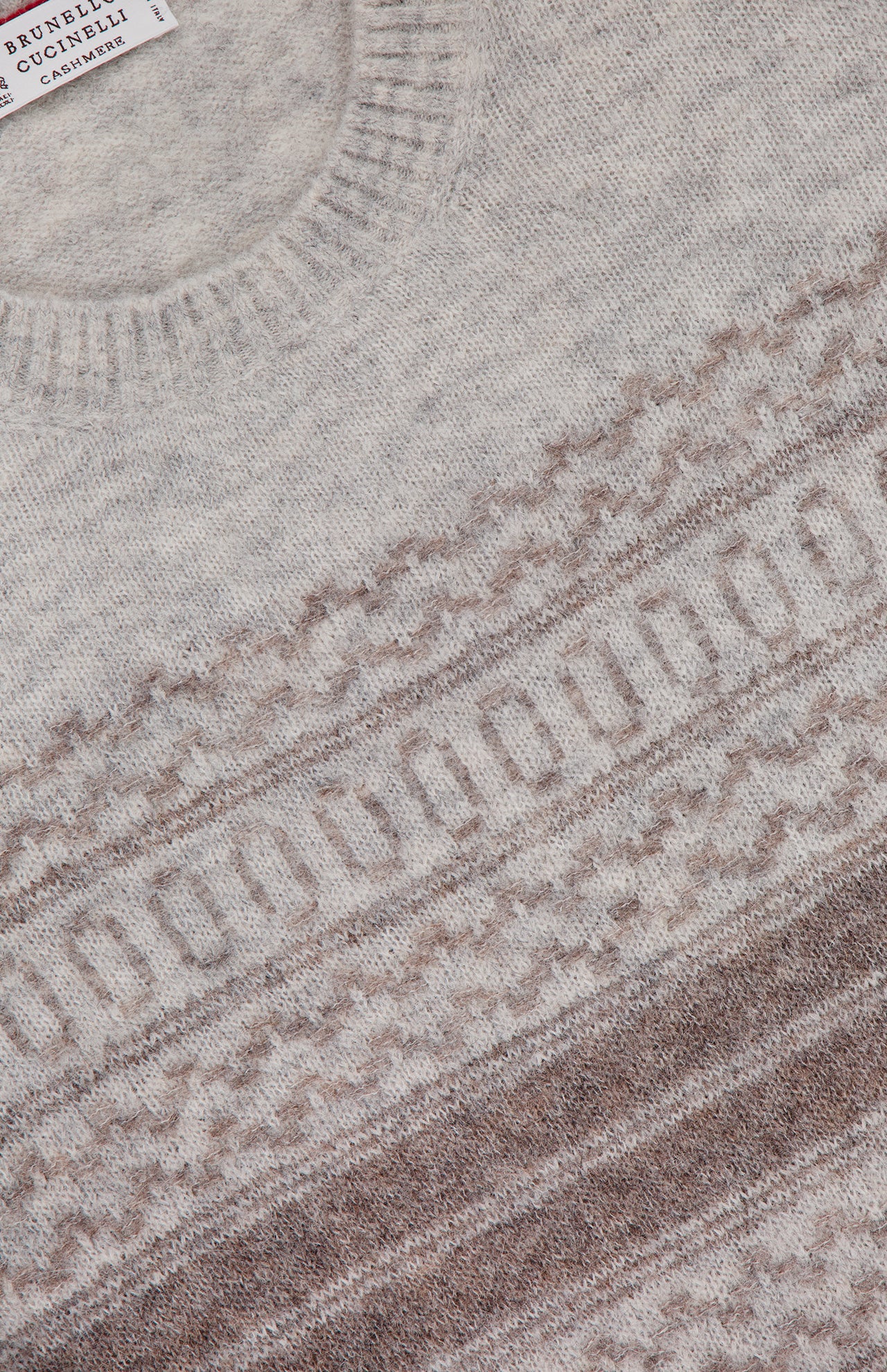 Close-up of a light beige BRUNELLO CUCINELLI Fair Isle Crewneck Sweater featuring intricate brown and cream geometric knit patterns across the chest. A portion of the BRUNELLO CUCINELLI label is visible near the collar.
