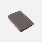 A closed Leather Passport and Cardholder by BRUNELLO CUCINELLI, crafted from brown leather with a subtle embossed logo in the corner, displayed on a plain white background.