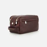 A brown Leather Dopp Kit by BRUNELLO CUCINELLI, crafted in Italy, featuring two zippered compartments, a front pocket, and a side handle embossed with the brand name in gold. This elegant travel accessory is displayed against a plain white background.