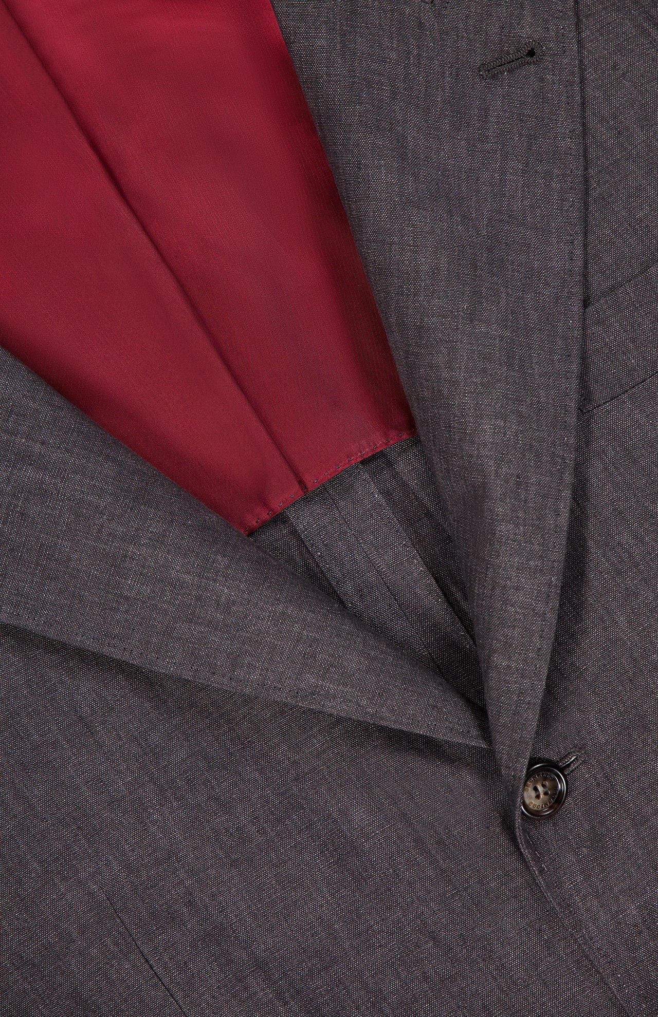 Close-up of the BRUNELLO CUCINELLI Linen Single-breasted Suit Jacket in dark grey, shown partially open to reveal its smooth red satin lining, a black button, and part of the lapel.