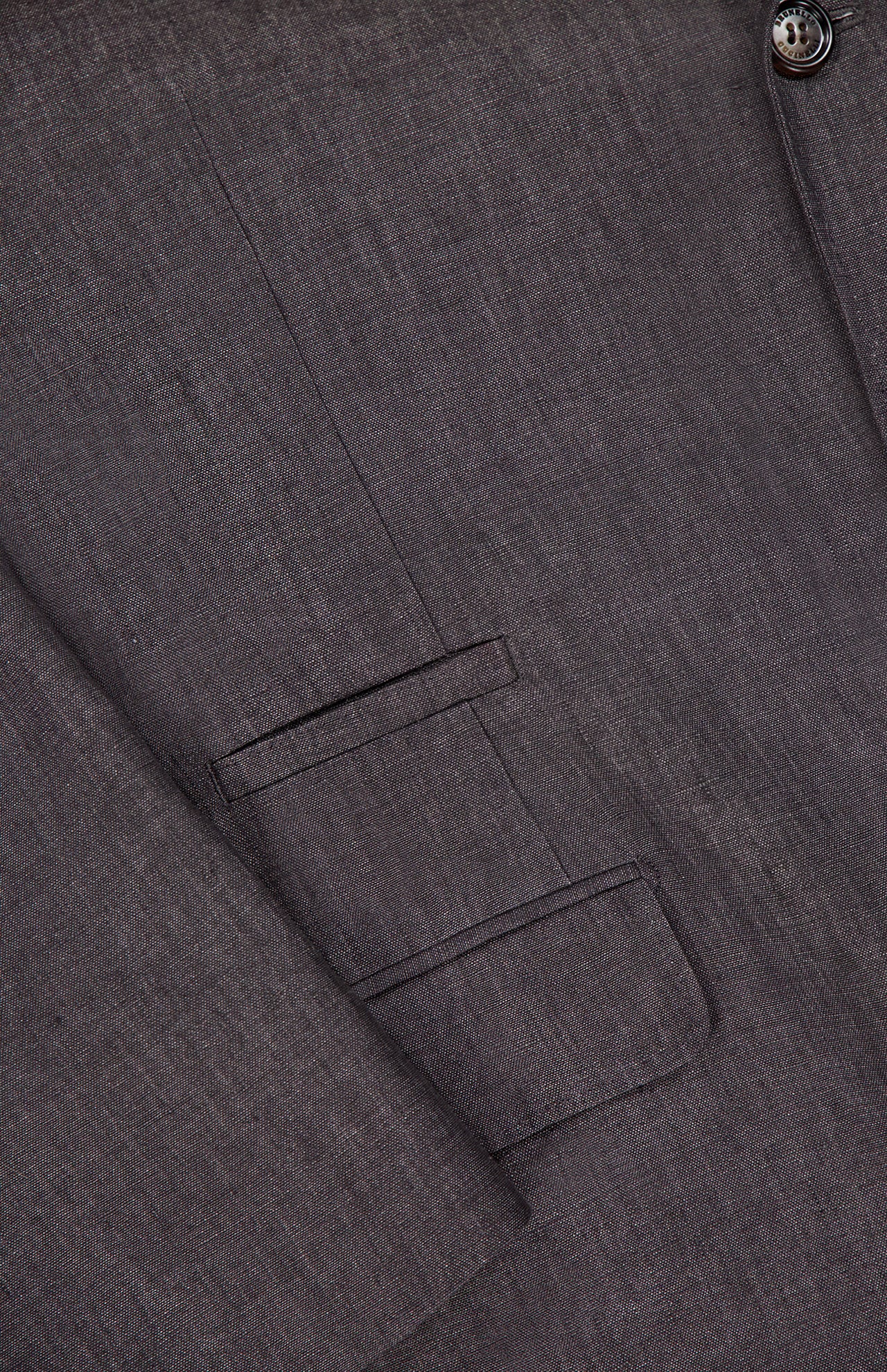 Close-up of the BRUNELLO CUCINELLI Linen Single-breasted Suit Jacket in dark brown textured fabric, highlighting the overlapping sleeve, flap pocket, and a button detail near the top right.