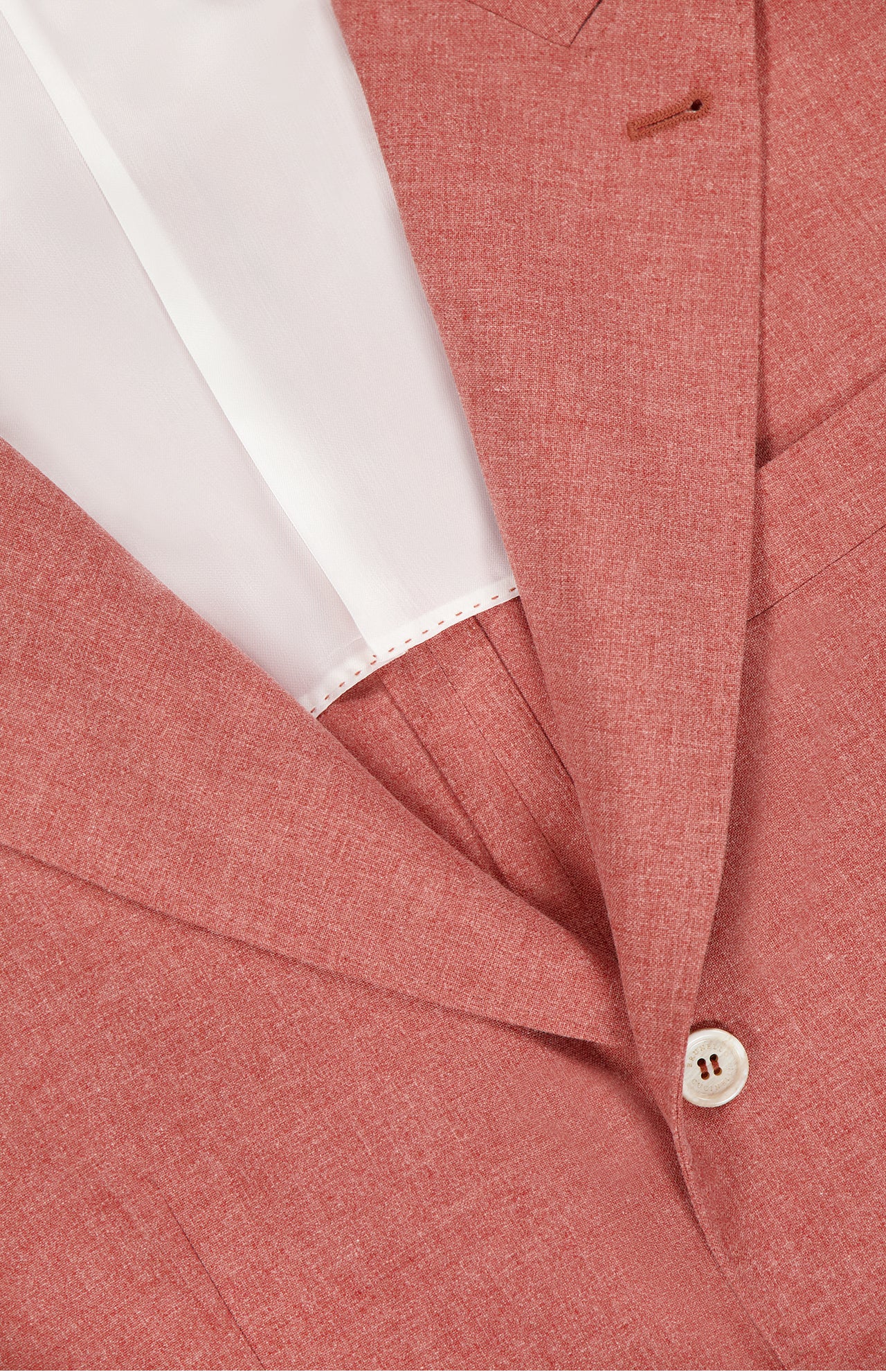 Close-up of a muted red BRUNELLO CUCINELLI sportcoat made in Italy from virgin wool, cotton, and silk. Features include a white button, white inner lining, notched lapel, and visible fabric texture.