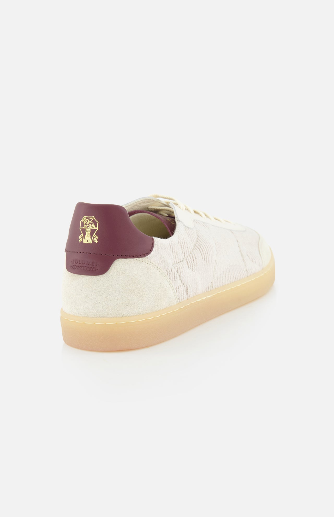 The BRUNELLO CUCINELLI Suede Leather Detailing Sneakers feature a cream-colored suede upper, white laces, tan gum sole, and a burgundy heel tab with a gold lion logo, shown from a rear side angle on a white background.