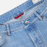 Close-up of light blue BRUNELLO CUCINELLI Traditional Fit Button Fly Jeans, highlighting the waistband, belt loops, button, front pockets, and a white label with brand name and size.