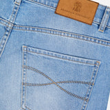 Close-up of the back pocket of light blue Traditional Fit Button Fly Jeans with tan stitching, featuring a brown leather BRUNELLO CUCINELLI label with a crest logo on the waistband.