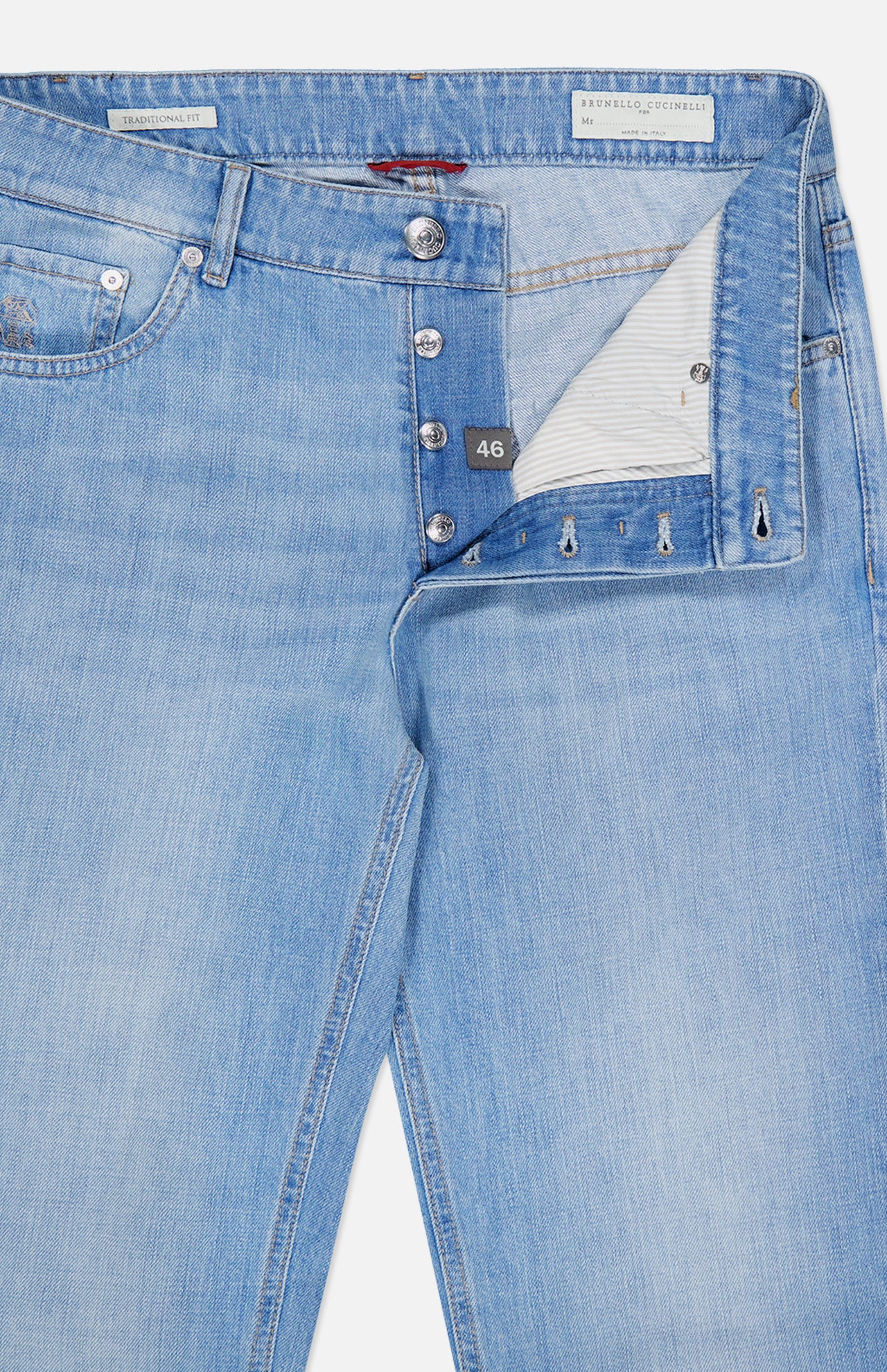 Introducing the Traditional Fit Light Denim jeans by BRUNELLO CUCINELLI: expertly crafted in Italy from premium light bluewash denim, these vintage-inspired jeans feature a partially open button fly revealing a striped inner waistband and a size 46 tag. Classic front pockets and signature visible stitching complete the timeless design.