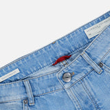 The Traditional Fit Light Denim jeans by BRUNELLO CUCINELLI are shown from the waist down at an angle, featuring a button closure, front pockets, and visible inside tags with text, including a label that reads BRUNELLO CUCINELLI. Crafted in Italy, these classic blue lightwash jeans offer timeless style.