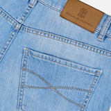 Close-up of the back pocket and waistband of the Traditional Fit Light Denim jeans by BRUNELLO CUCINELLI in light blue wash, featuring a brown leather brand patch above the pocket and distinctive stitching detail. Crafted from premium lightwash denim, these jeans showcase vintage-inspired style.