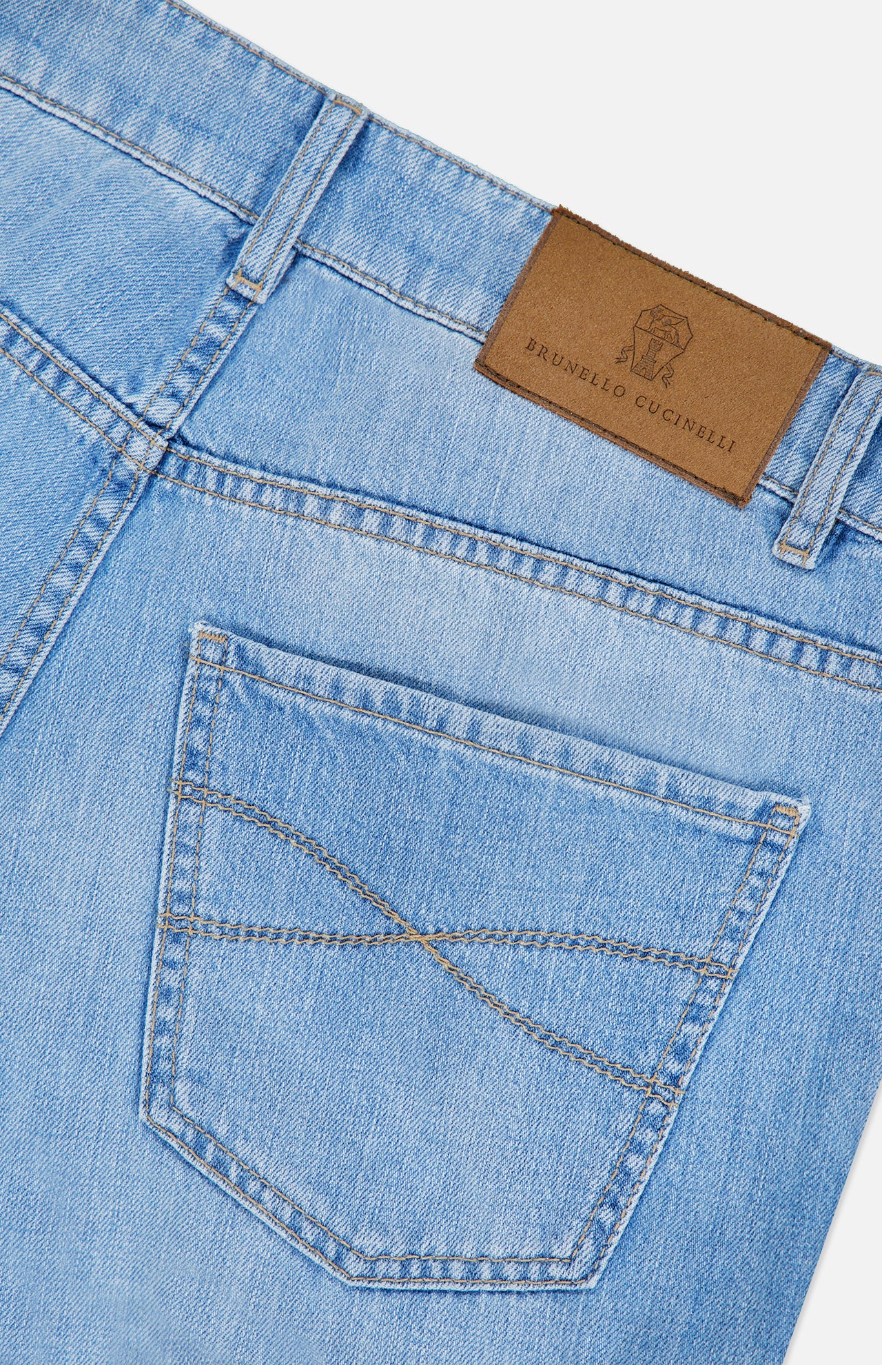 Close-up of the back pocket and waistband of the Traditional Fit Light Denim jeans by BRUNELLO CUCINELLI in light blue wash, featuring a brown leather brand patch above the pocket and distinctive stitching detail. Crafted from premium lightwash denim, these jeans showcase vintage-inspired style.