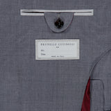 Detailed close-up of the inner pocket on the grey BRUNELLO CUCINELLI Wool and Silk Travel Blazer, showcasing a button closure and a Brunello Cucinelli label with spaces for “Mr.” and “Date,” along with the inscription “Made in Italy.” The partially visible lining is red.