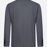 The BRUNELLO CUCINELLI Wool and Silk Travel Blazer is displayed from the back, showcasing its gray single-breasted design, long sleeves, and black cuff buttons against a plain white background. Crafted from a luxurious blend of wool and silk, this blazer exemplifies classic tailoring and sophistication, ensuring versatile wear for any occasion.