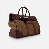 The BRUNELLO CUCINELLI Travel Duffle Bag with Chevron-effect showcases large brown leather accents paired with herringbone-patterned fabric panels for a refined, country-inspired look. Featuring two handles, a flap closure with metal hardware, and a structured silhouette, the bag is elegantly displayed against a plain white background.