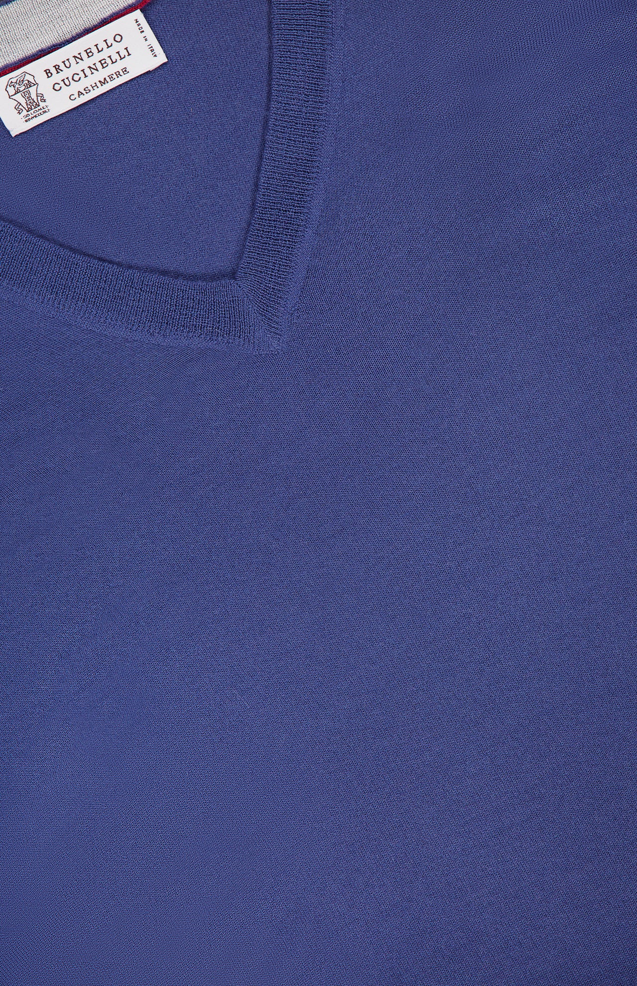 Close-up of the V-Neck Wool Cashmere Sweater in blue, showcasing its fine knit texture and classic V-neck design. The label in the top left corner displays the BRUNELLO CUCINELLI brand name, highlighting the luxurious quality of this wool cashmere piece.
